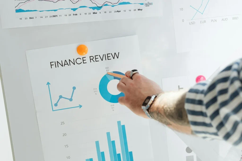 Tangan menunjuk grafik keuangan berwarna dalam presentasi bisnis di ruang rapat