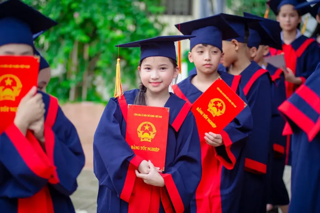 Anak-anak mengenakan toga kelulusan memegang ijazah saat acara perpisahan sekolah